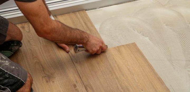 Installer cutting and fitting a wood-look LVP plank over freshly spread self-leveling compound; trowel marks visible on subfloor—demonstrating proper substrate prep for floating-floor installations.