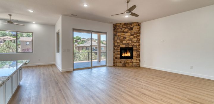 Spacious, newly finished living area featuring light gray-washed luxury vinyl plank flooring, white walls, recessed lighting, stone-clad fireplace with gas insert, and sliding glass doors to an outdoor patio.