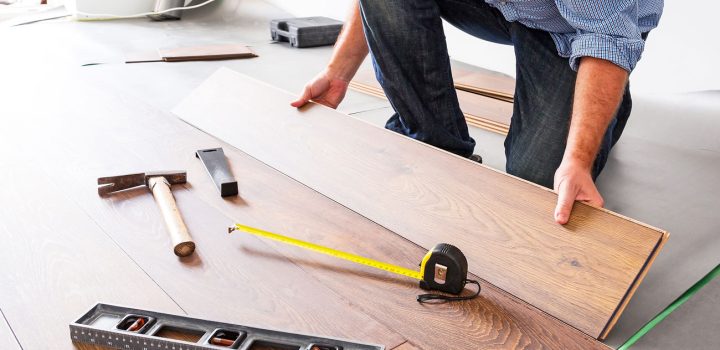 A contractor installing engineered hardwood planks on a subfloor; tools including tape measure, level, tapping block, and hammer are laid out nearby—highlighting craftsmanship and attention to detail.