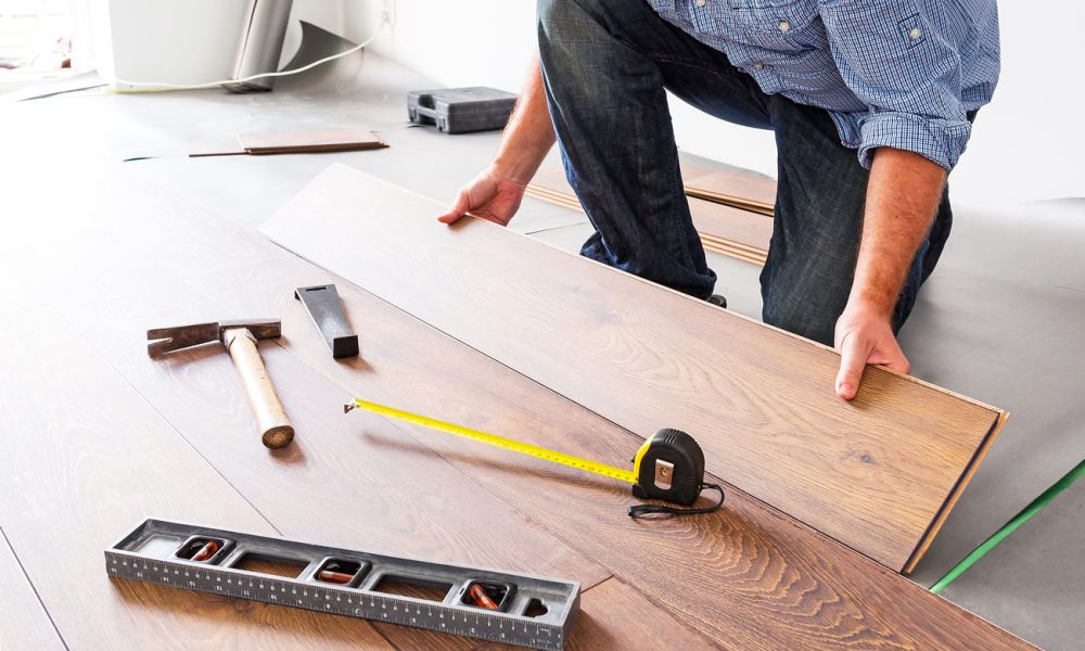 A contractor installing engineered hardwood planks on a subfloor; tools including tape measure, level, tapping block, and hammer are laid out nearby—highlighting craftsmanship and attention to detail.